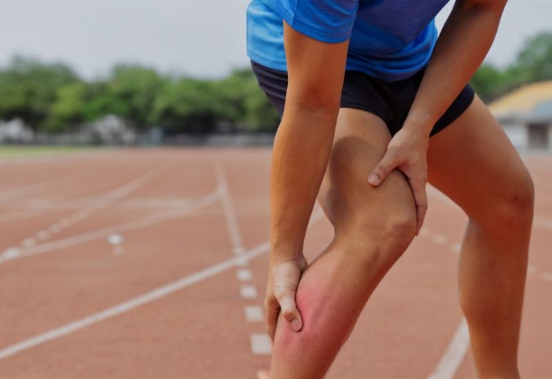 Corredor con gesto de dolor agudo parado en la pista tras sentir un chasquido muscular compatible con un desgarro o rotura fibrilar.