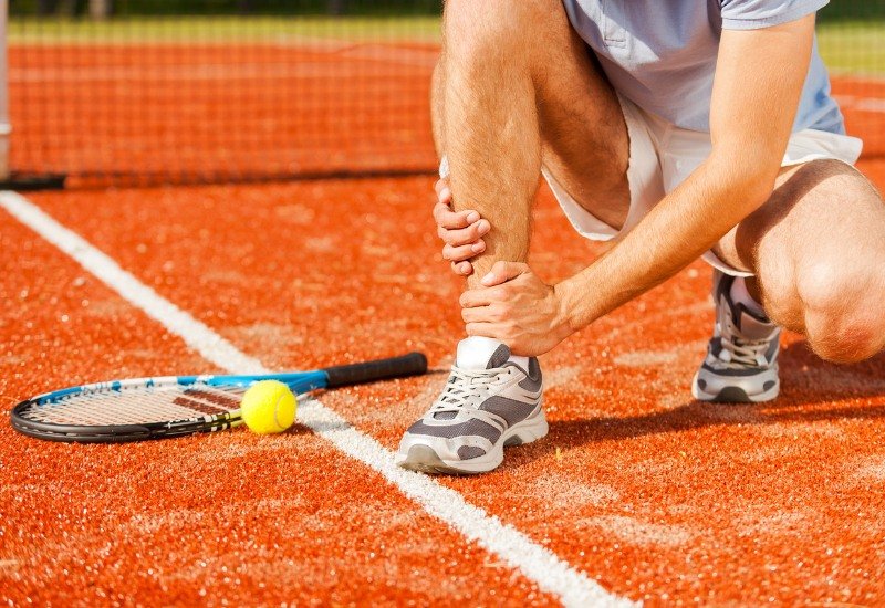 Deportista sufriendo una lesión deportiva en la rodilla durante un partido de tenis, tratada mediante fisioterapia avanzada en el Actur.