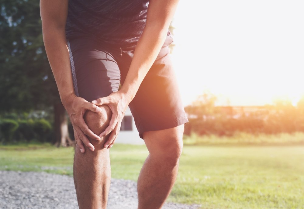 Deportista sufriendo un dolor agudo de rodilla por un esguince o lesión deportiva tras entrenar.